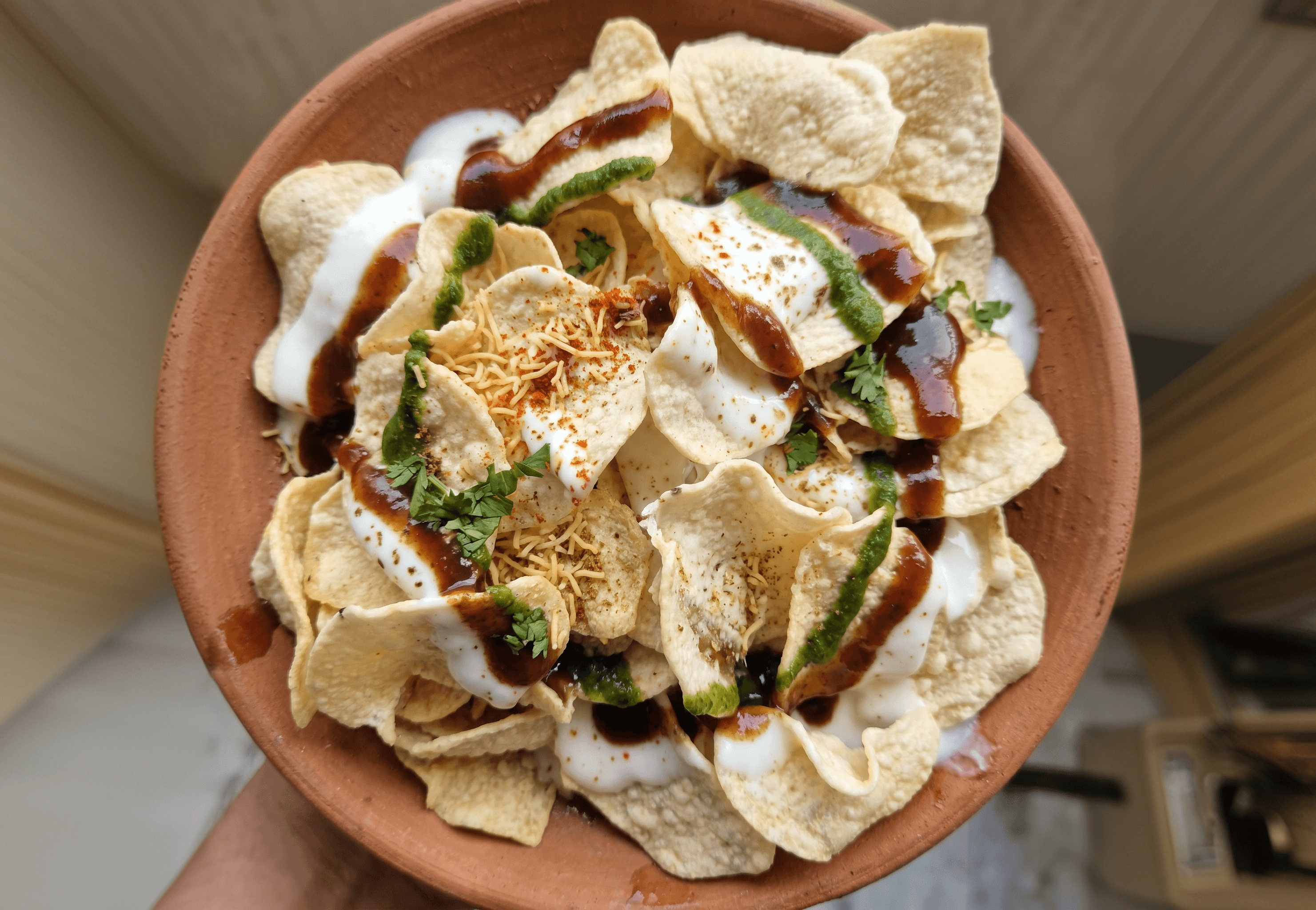 A bowl of street-style chaat topped with yogurt, chutney and herbs
